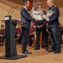 Bürgermeister Manuel Follmann überreicht Stephan Christ im Beisein des stellvertretenden Wehrleiters Dirk Minor das Geschenk der Verwaltung